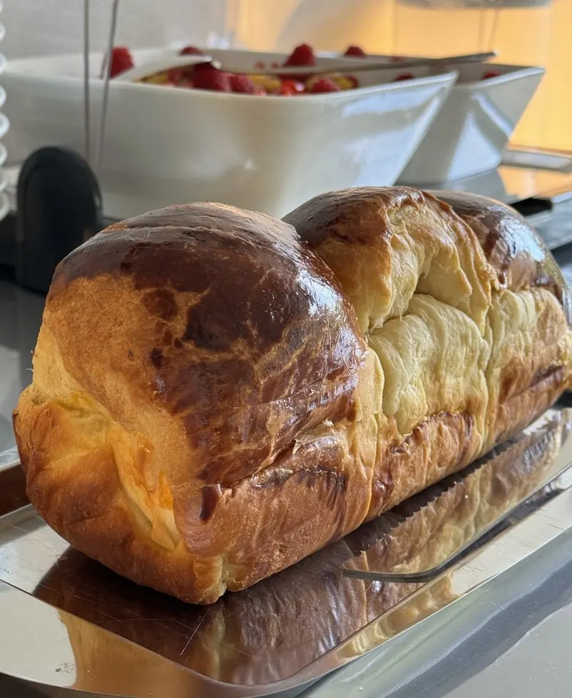 Golden homemade brioche on a tray in front of dishes of raspberries at breakfast, Le 36