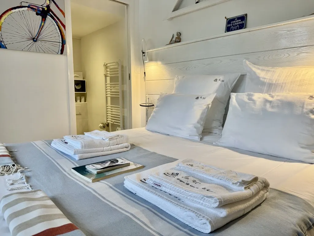 La Cabine bedroom at Le 36: white bed, striped throw, folded towels, wooden headboard and bicycle print