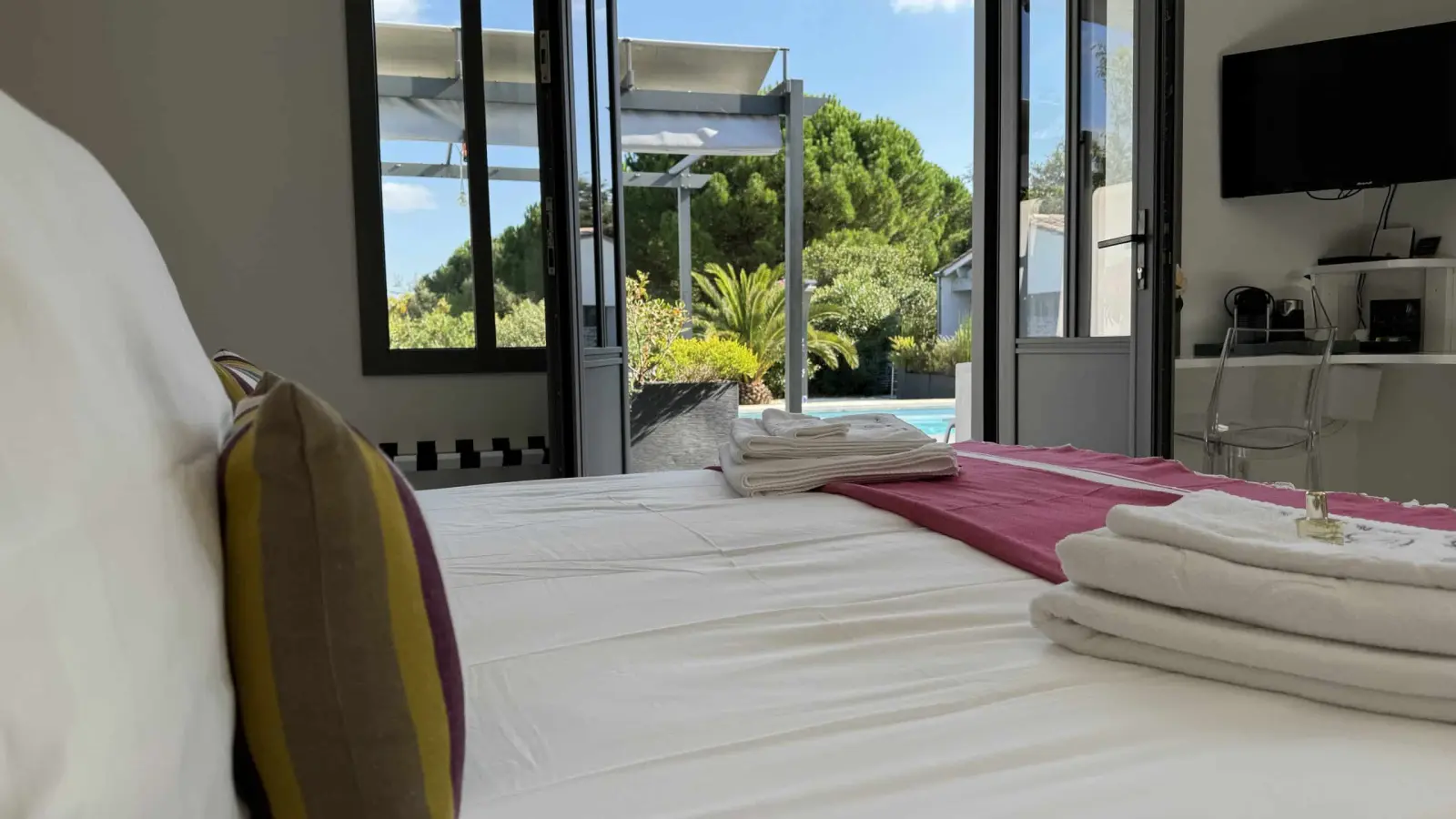 Les Bouées bedroom at Le 36 seen from the bed, doors open to the pool, towels and a pink bed runner
