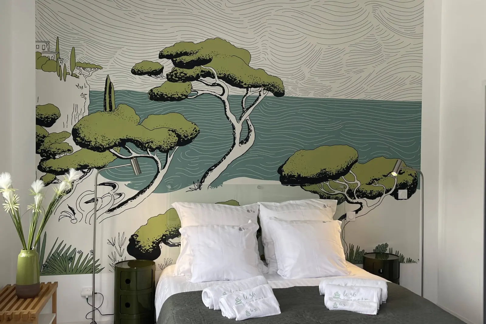 Les Embruns bedroom at Le 36: double bed beneath a mural of pines and sea, rolled towels and a vase