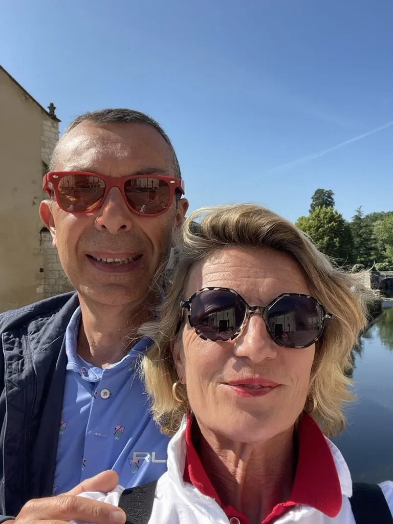 The hosts of Le 36, a smiling couple in sunglasses, taking a selfie by a river under a blue sky