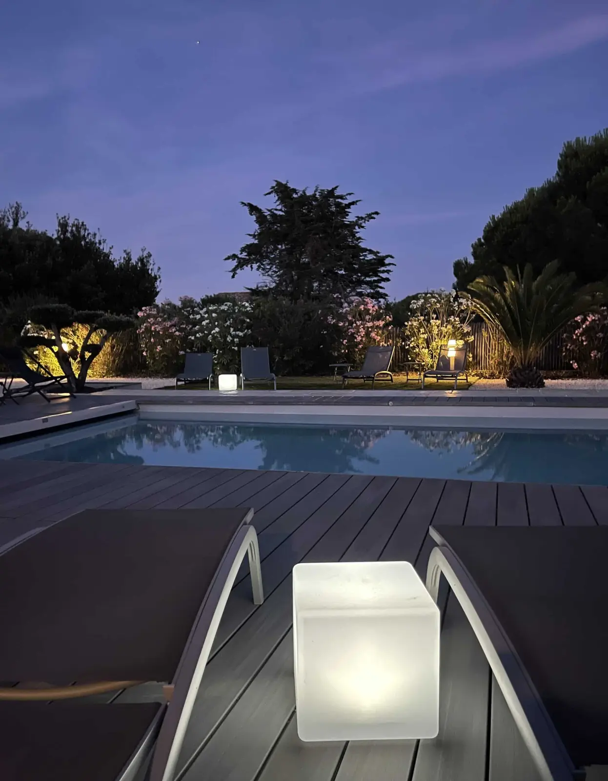 Pool at Le 36 at dusk, sun loungers on the wooden deck, a glowing cube lamp and a lit garden