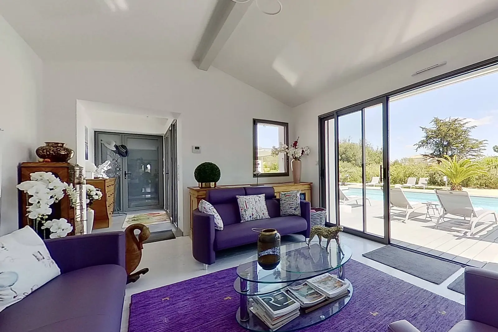 Lounge at Le 36 with purple sofas, glass coffee table, purple rug and glass doors open onto the pool