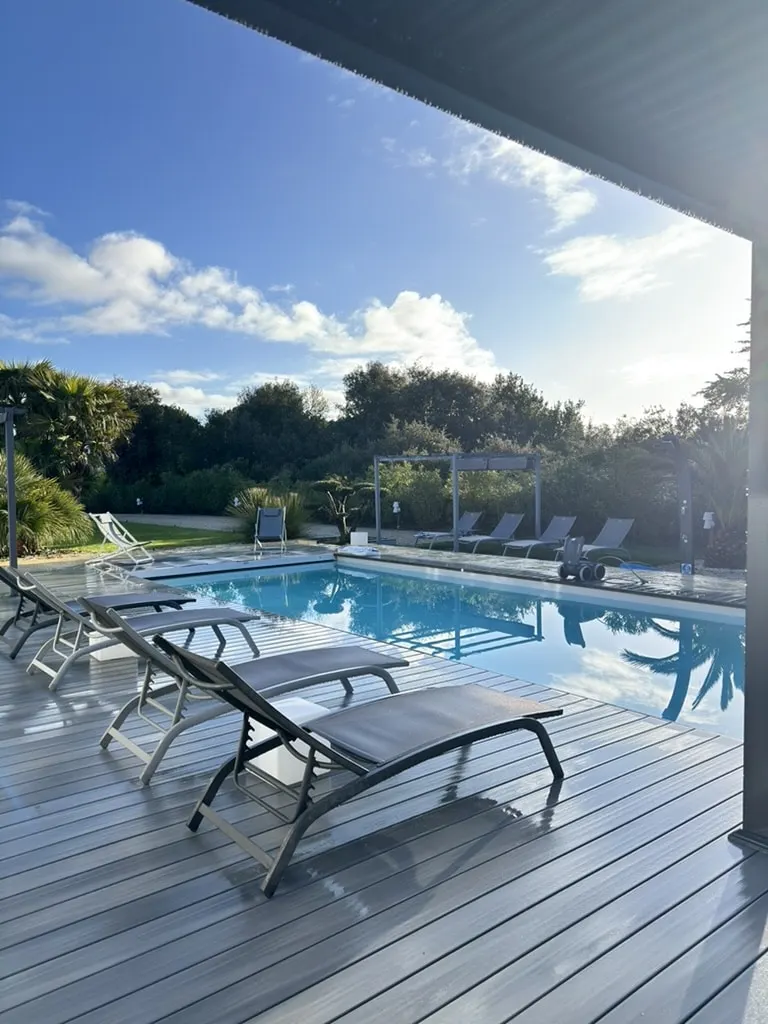 Sun loungers lined up on the covered wooden deck facing the pool and wooded garden at Le 36