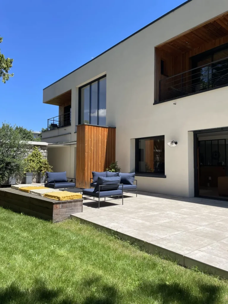 Contemporary house with timber cladding, a terrace, blue garden furniture and a sunny lawn