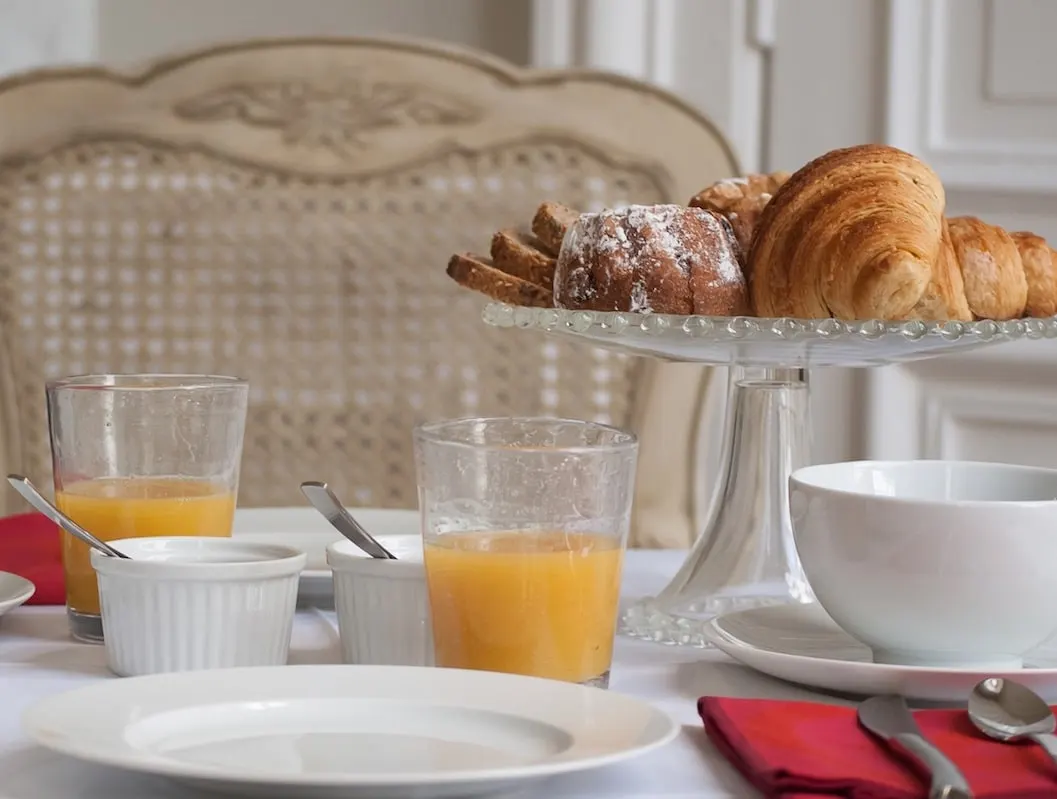 Petit-déjeuner de La Maison M : croissants et brioche sur présentoir en verre, jus d'orange et vaisselle blanche