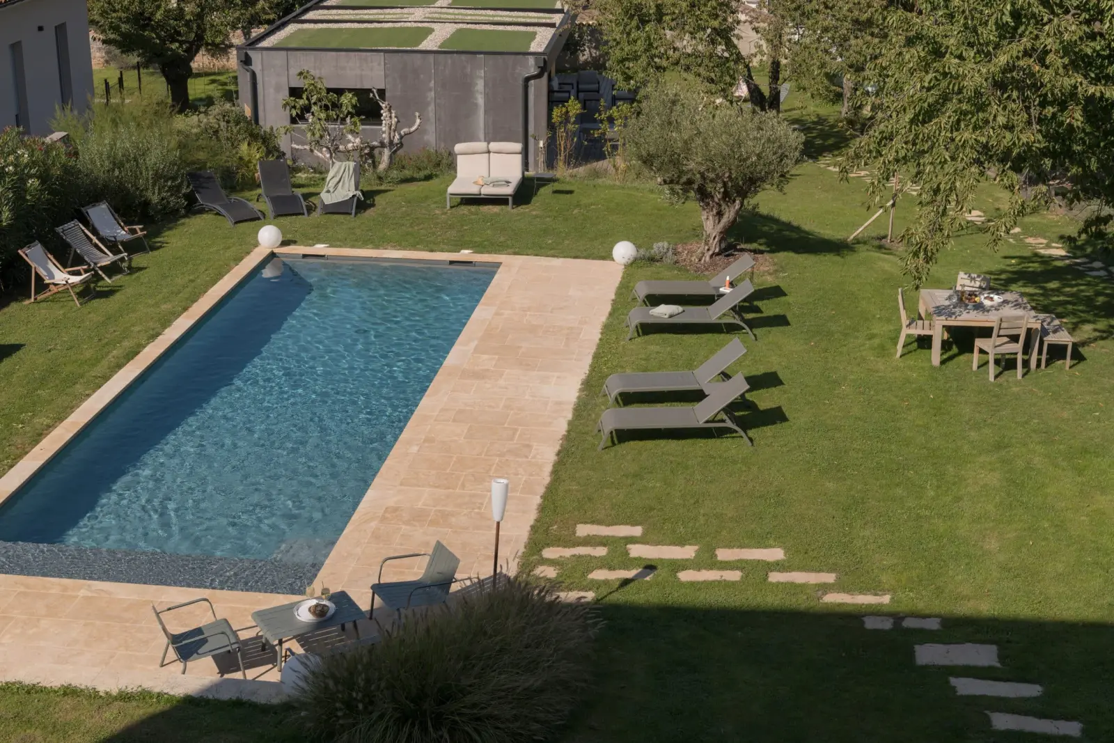 Piscine de La Maison des Monts d'Or bordée de dalles claires, transats et table sur la pelouse