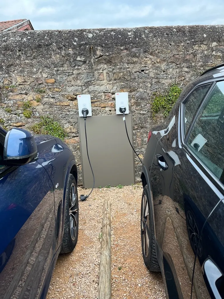Two electric car charging points on a stone wall between two parked cars, La Maison des Monts d'Or