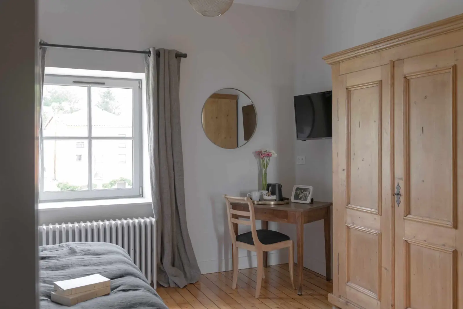 Bedroom at La Maison des Monts d'Or with a pale wooden wardrobe, desk, round mirror and bright window
