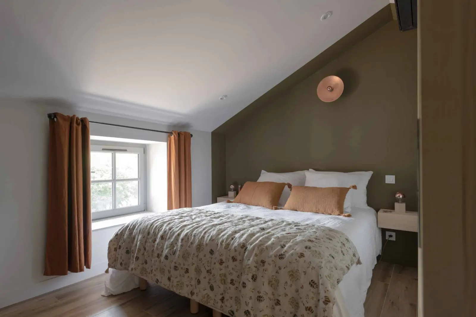 Attic bedroom in the gîte: double bed with a floral bedspread, russet cushions and curtains, La Maison des Monts d'Or