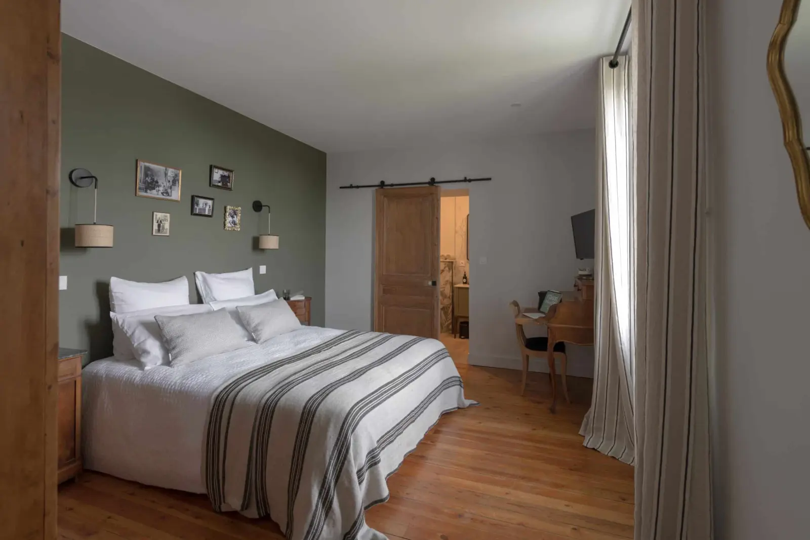 Bedroom at La Maison des Monts d'Or: double bed, green wall with framed photos and a sliding wooden door