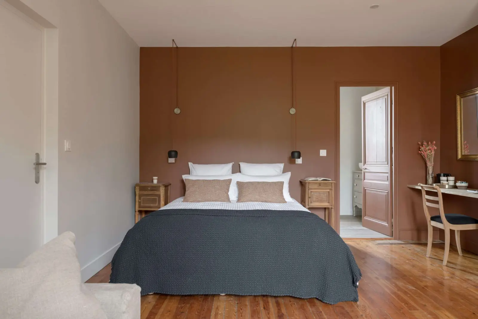 Terracotta-walled bedroom at La Maison des Monts d'Or: double bed with a grey bedspread and wooden floor
