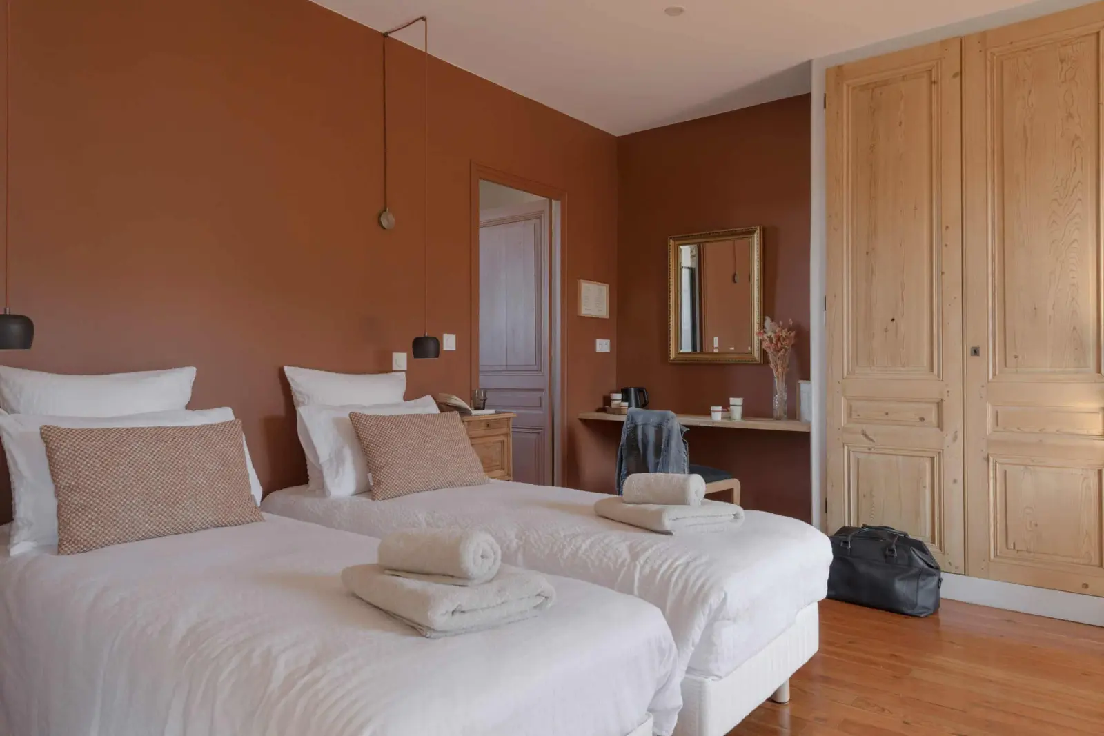 Terracotta-walled bedroom at La Maison des Monts d'Or: two single beds, gilt mirror and wooden cupboard
