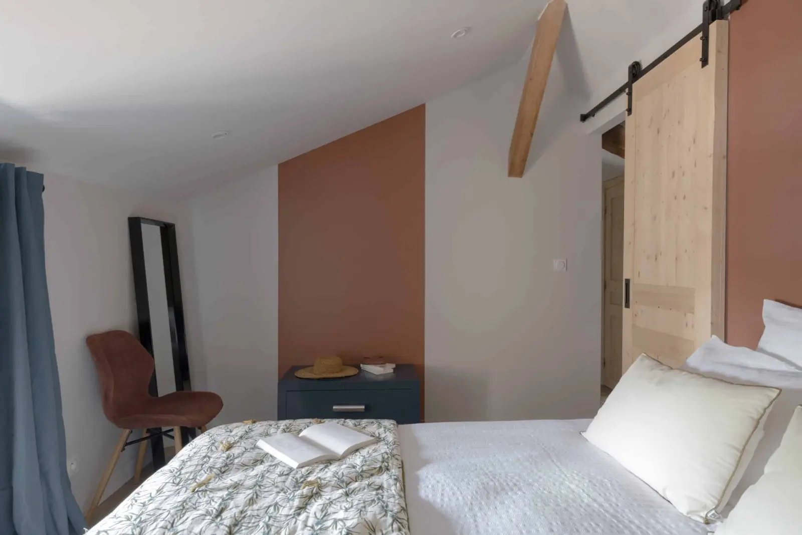 Attic bedroom with a double bed, terracotta wall and sliding wooden barn door, La Maison des Monts d'Or