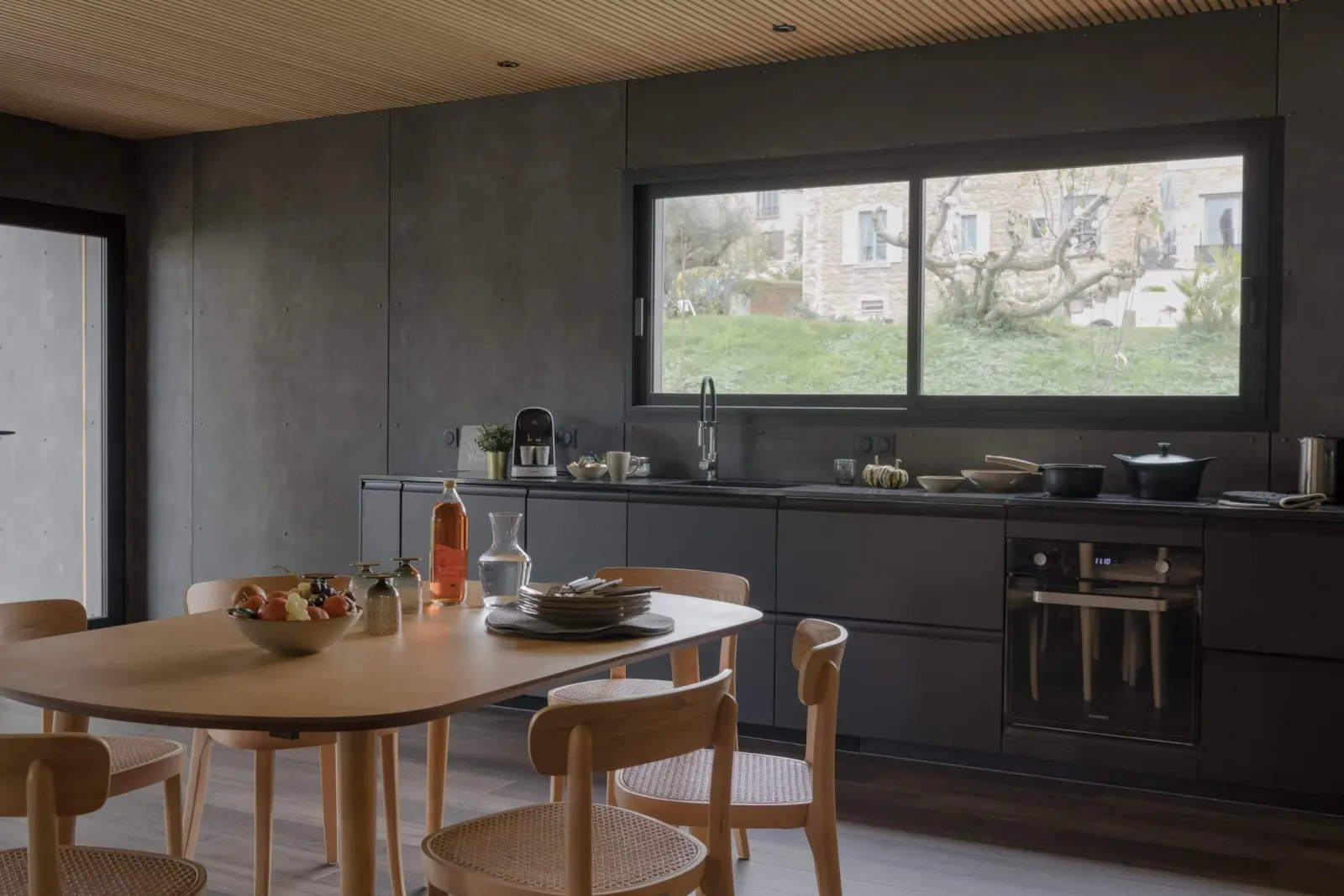Black kitchen with a wooden table and a wide window onto the garden, gîte at La Maison des Monts d'Or