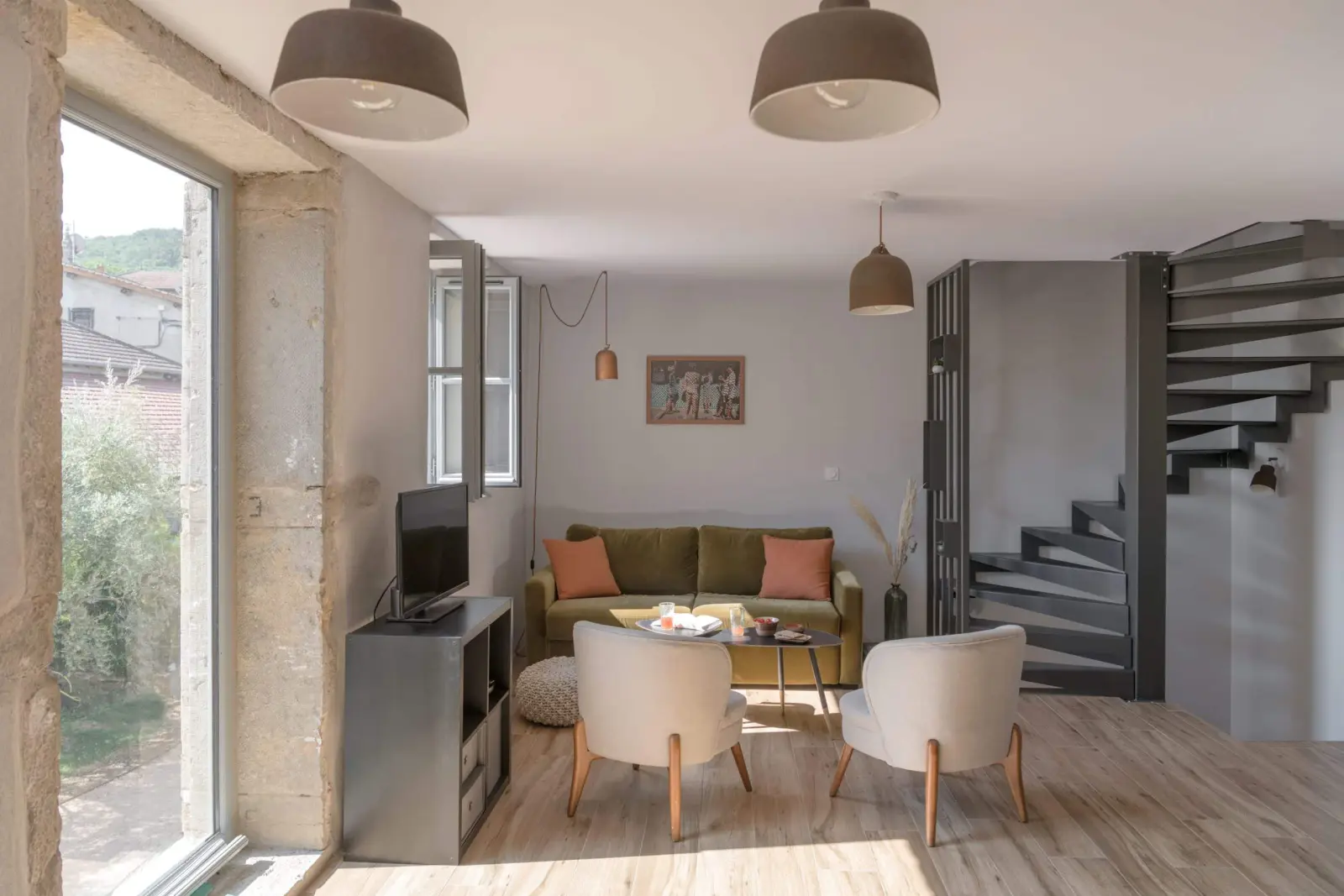 Gîte sitting room: green sofa, white armchairs, pendant lights and spiral staircase, La Maison des Monts d'Or