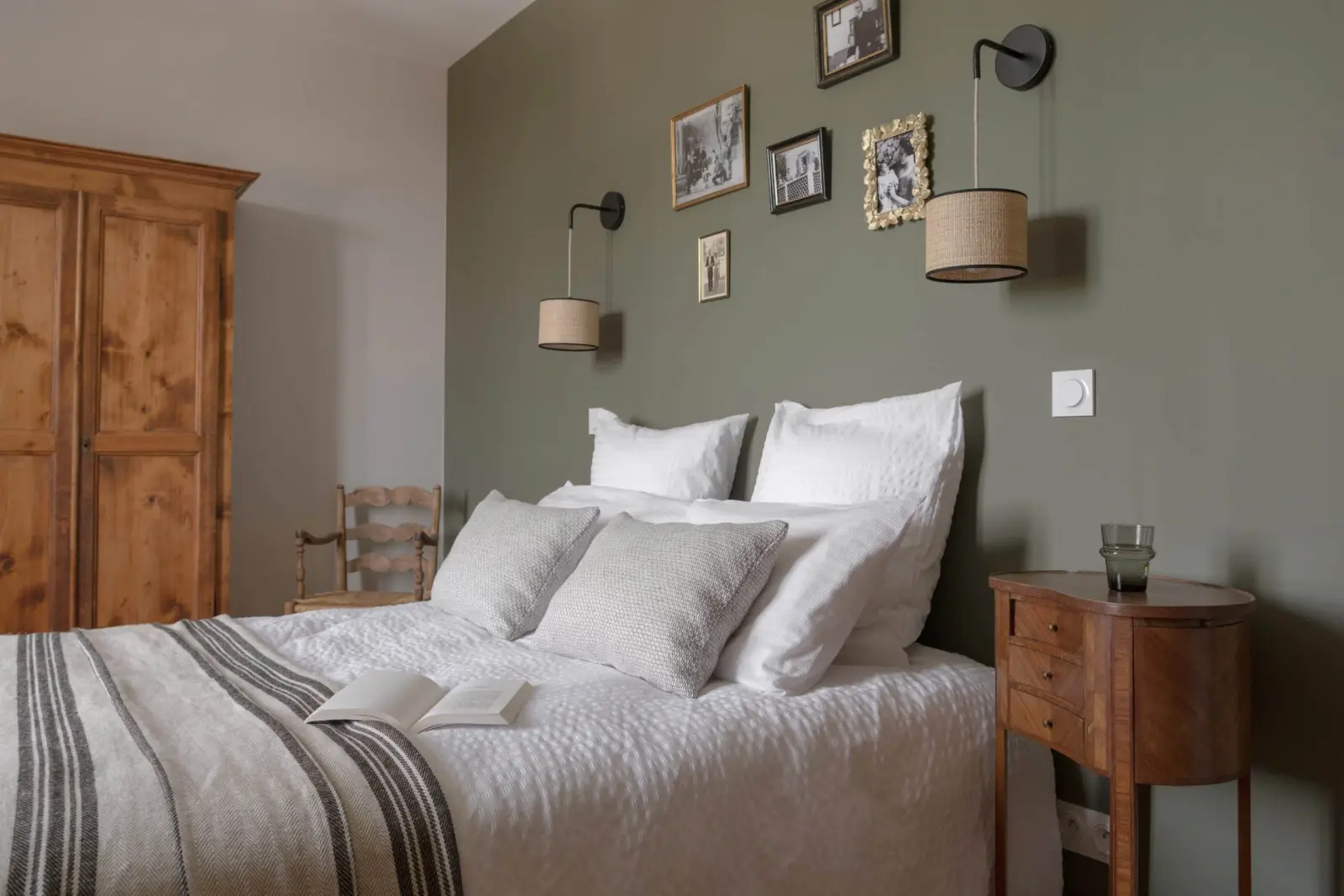 Double bed against a green wall hung with frames and rattan wall lights, wooden wardrobe, La Maison des Monts d'Or