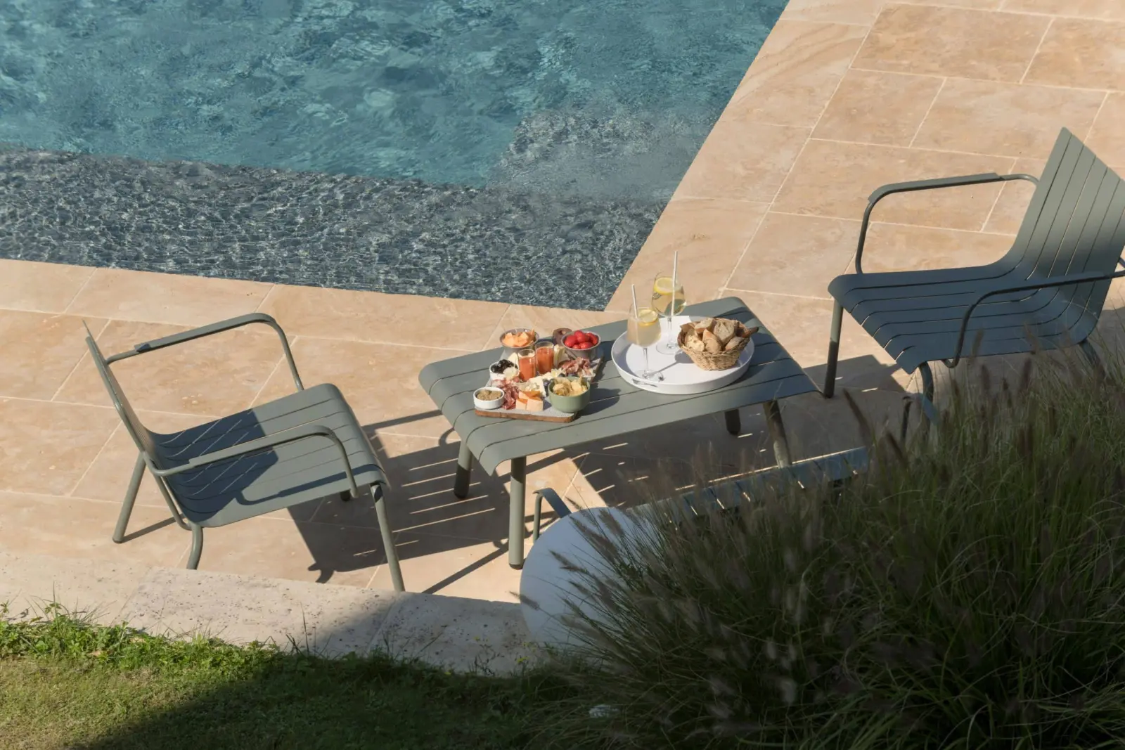 Low table set with aperitif nibbles between two green chairs by the pool, La Maison des Monts d'Or