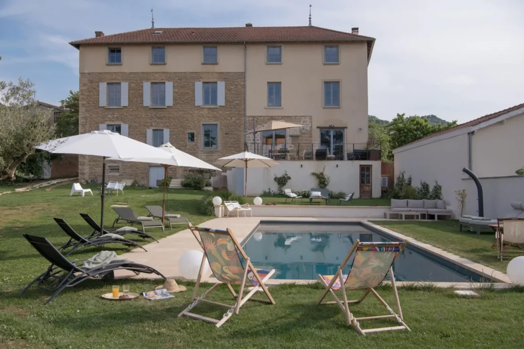 Stone and rendered house, pool and lawn with sun loungers, deckchairs and white parasols, La Maison des Monts d'Or