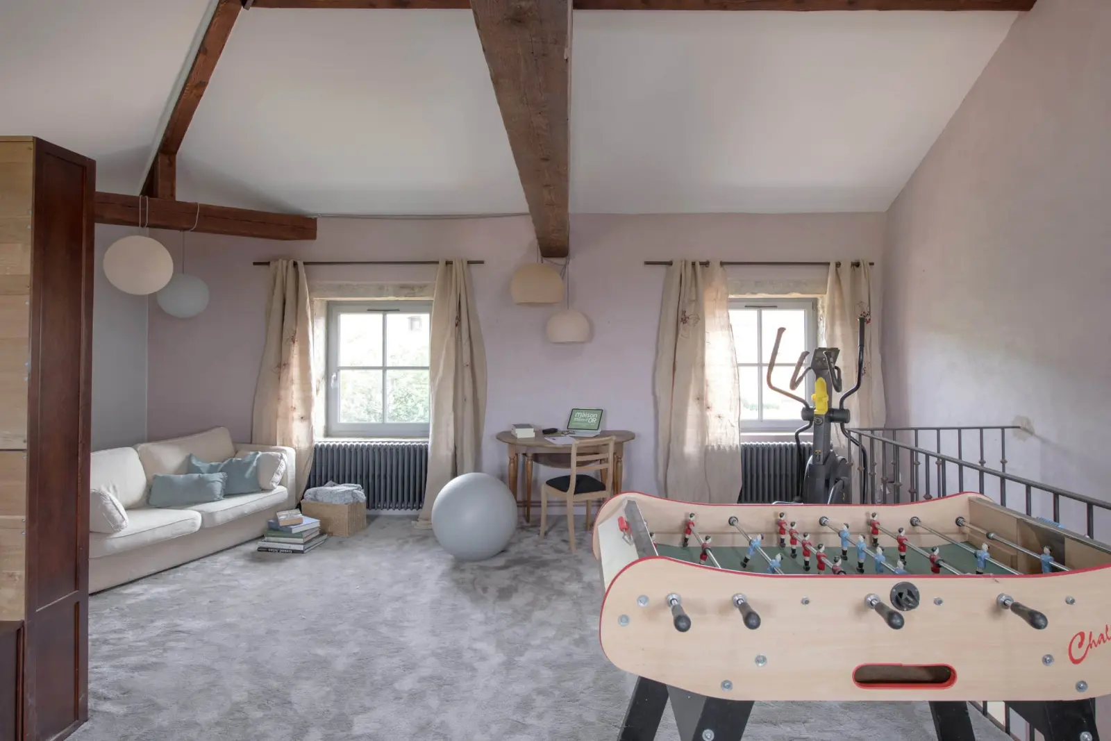Games room under exposed beams at La Maison des Monts d'Or: table football, sofa, desk and cross-trainer