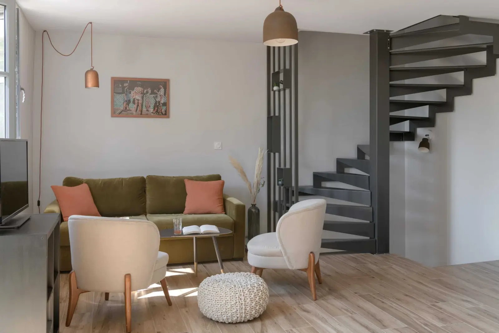 Sitting room with a green sofa and orange cushions, white armchairs, pouffe and spiral staircase, La Maison des Monts d'Or