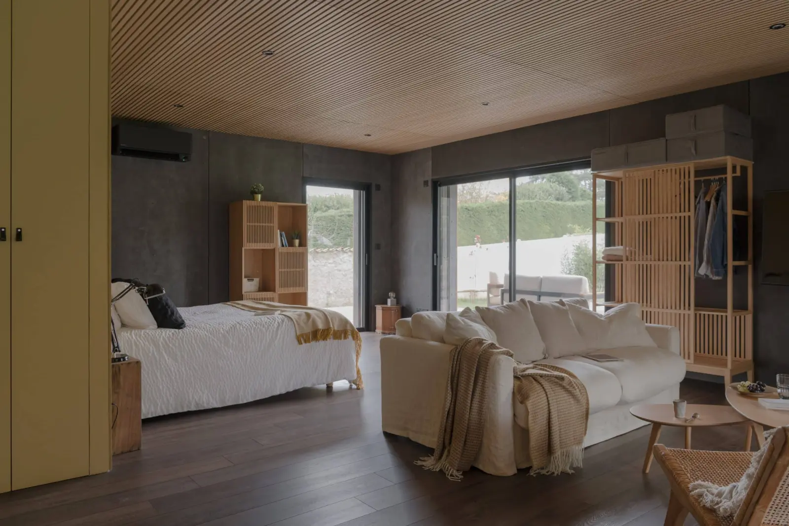 Studio at La Maison des Monts d'Or with a bed, white sofa, slatted wooden ceiling and glass doors