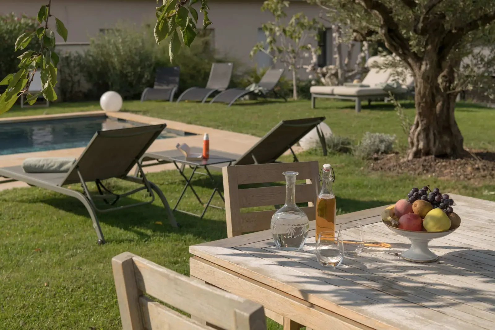 Wooden table with fruit and carafes near the pool, sun loungers and an olive tree, La Maison des Monts d'Or