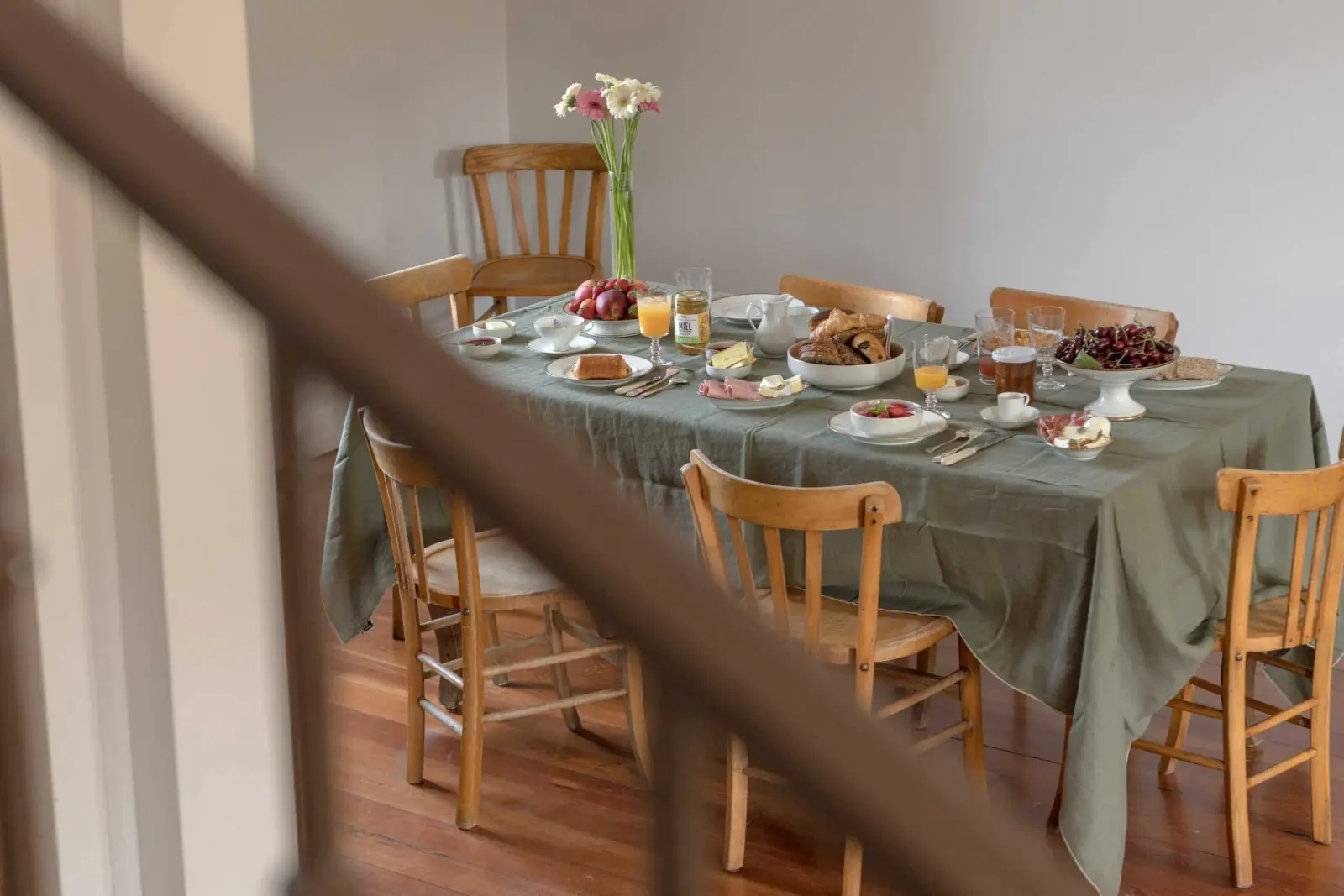 Large breakfast table laid with a green cloth, fruit, pastries and wooden chairs, La Maison des Monts d'Or