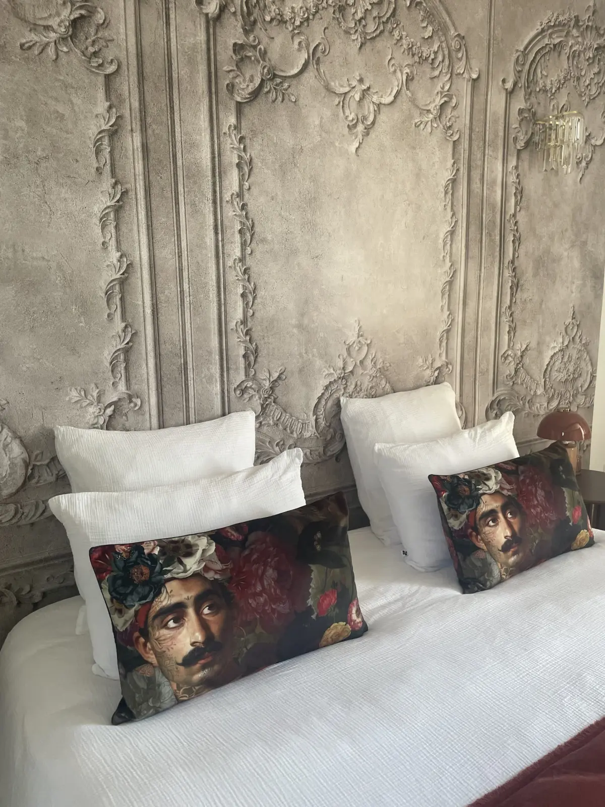 Bed in the Deauville room at Domaine de Marculfo, floral portrait cushions against moulding-effect wallpaper