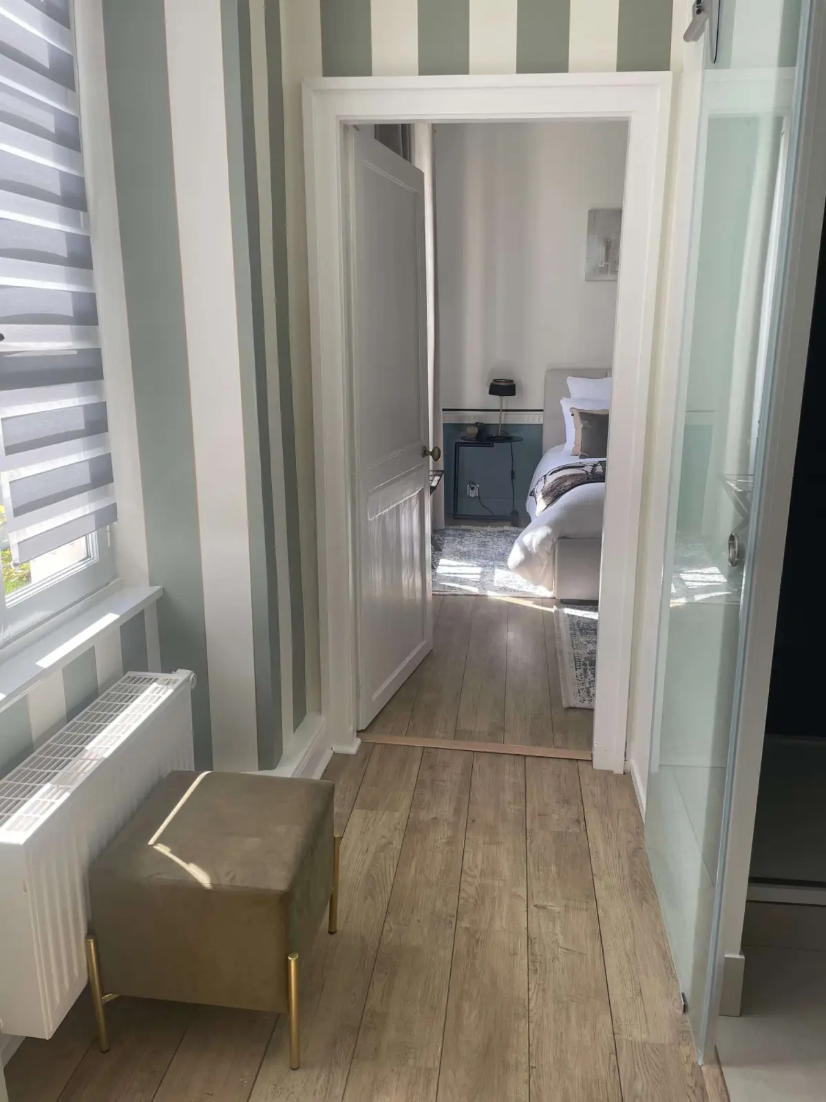 Entrance to the Honfleur room at Marculfo, sage-striped walls, velvet pouf and door open onto the bed