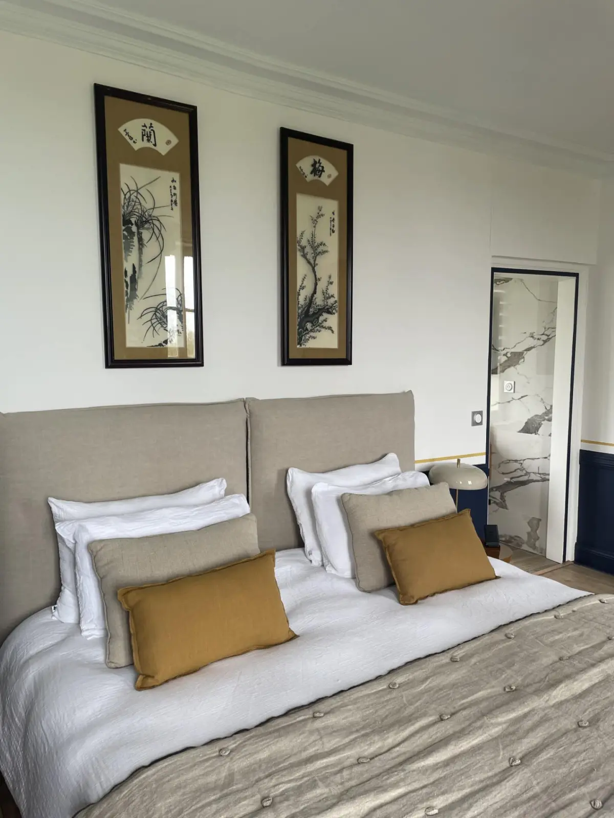 Bed in the Houlgate room at Marculfo, linen headboard, mustard cushions and two Asian prints