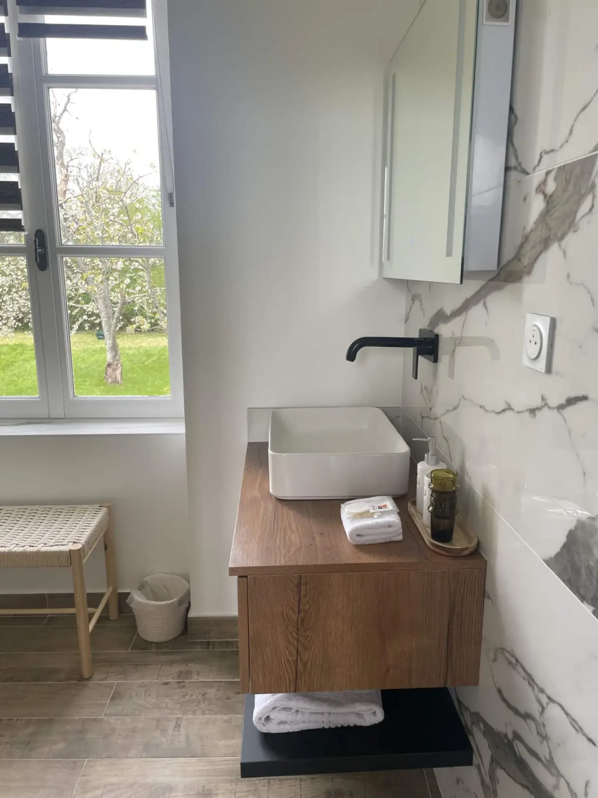 Bathroom of the Houlgate room at Marculfo, basin on a wooden unit, marble-effect wall and garden window