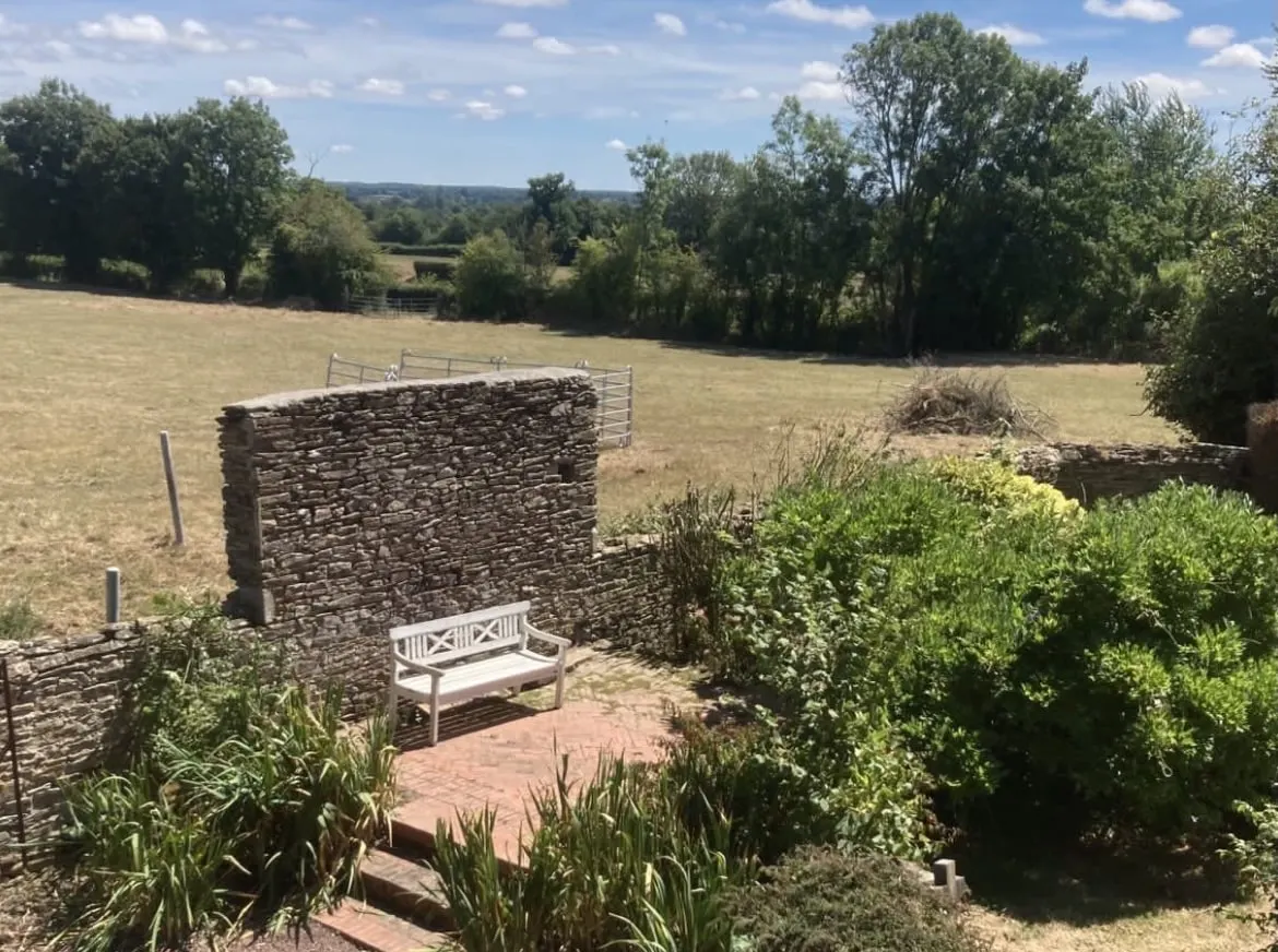 Garden at Domaine de Marculfo with white bench and dry-stone wall, opening onto a meadow and trees