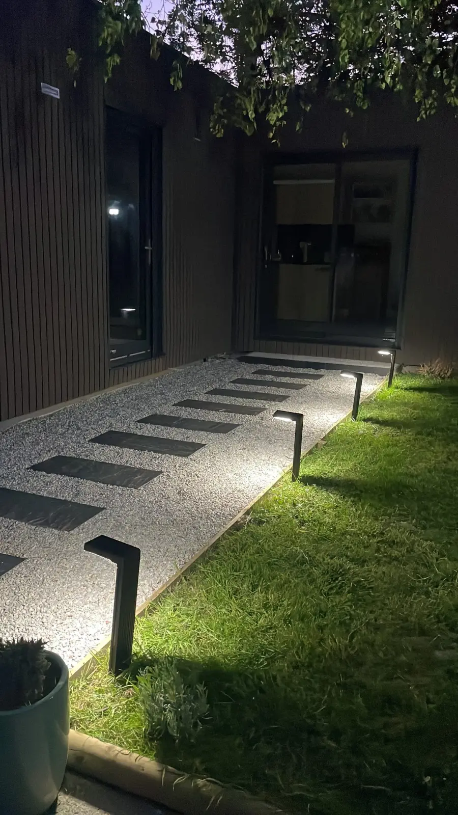 Lodge path at Domaine de Marculfo lit by bollards at night, between lawn and dark cladding