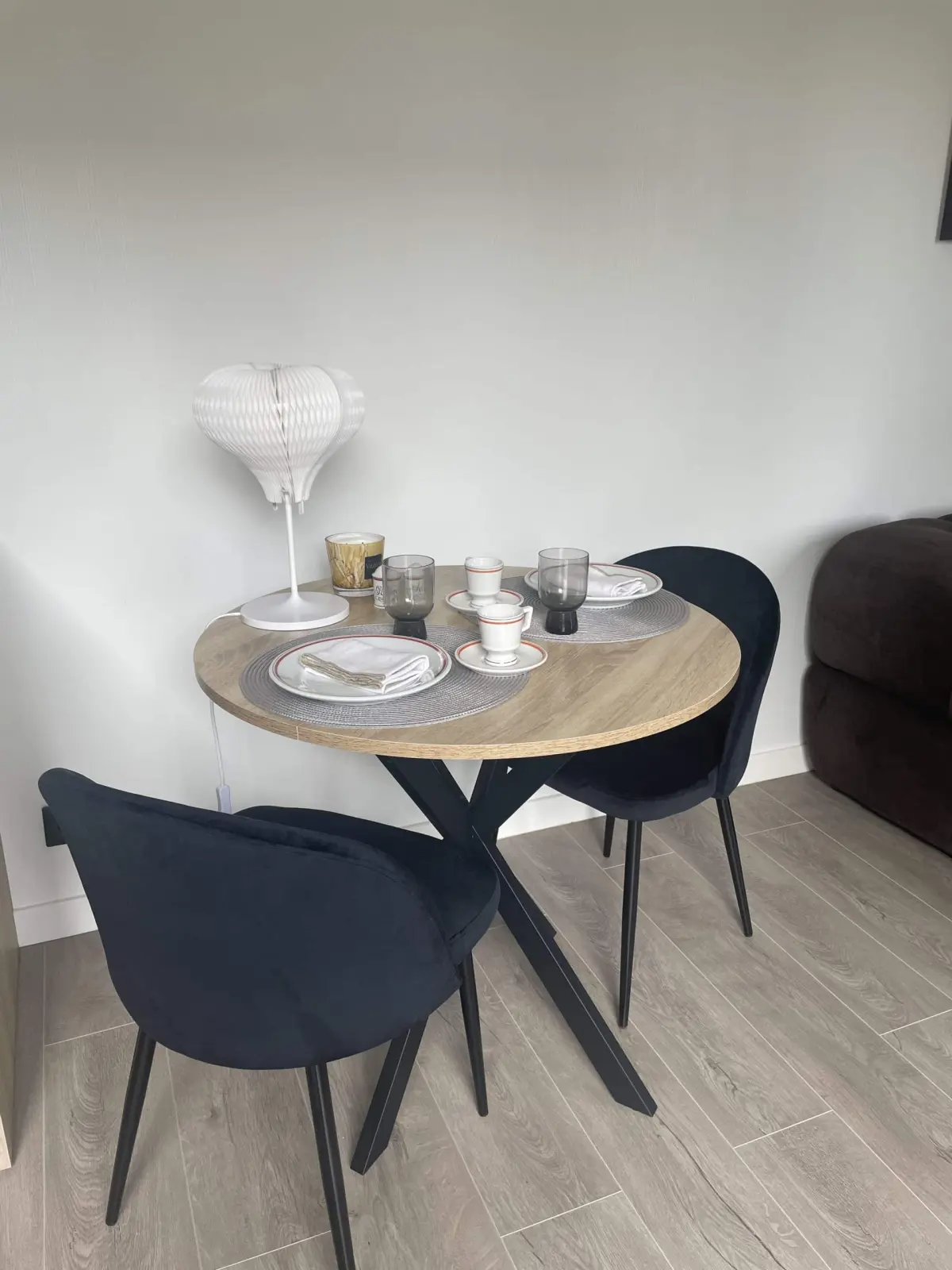 Dining corner of the lodge at Domaine de Marculfo, round wooden table laid, black velvet chairs and lamp