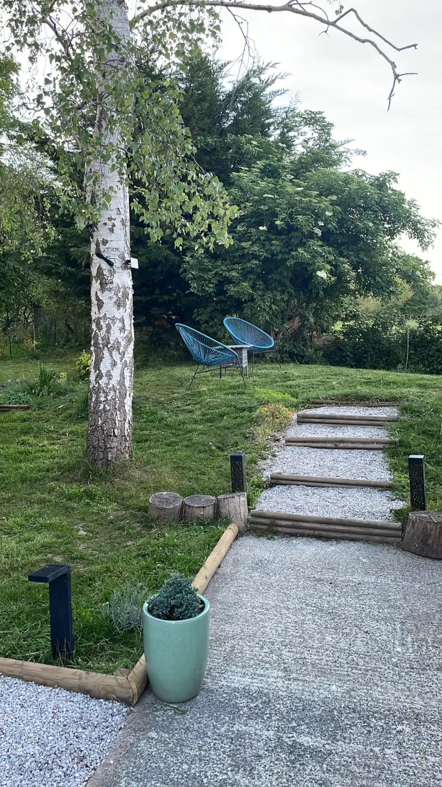Lodge garden at Domaine de Marculfo: birch tree, gravel steps and two blue chairs on the lawn