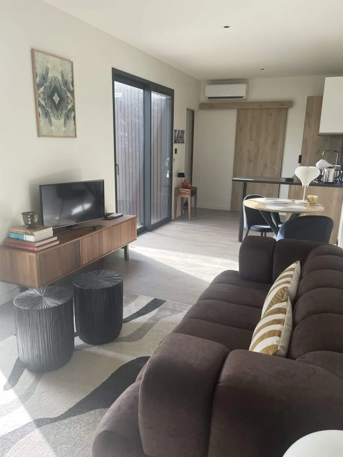 Living area of the lodge at Domaine de Marculfo, brown sofa, television, dining corner and kitchen beyond