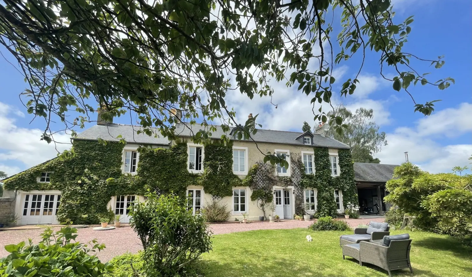Ivy-covered facade of Domaine de Marculfo, tall white windows, lawn and garden furniture