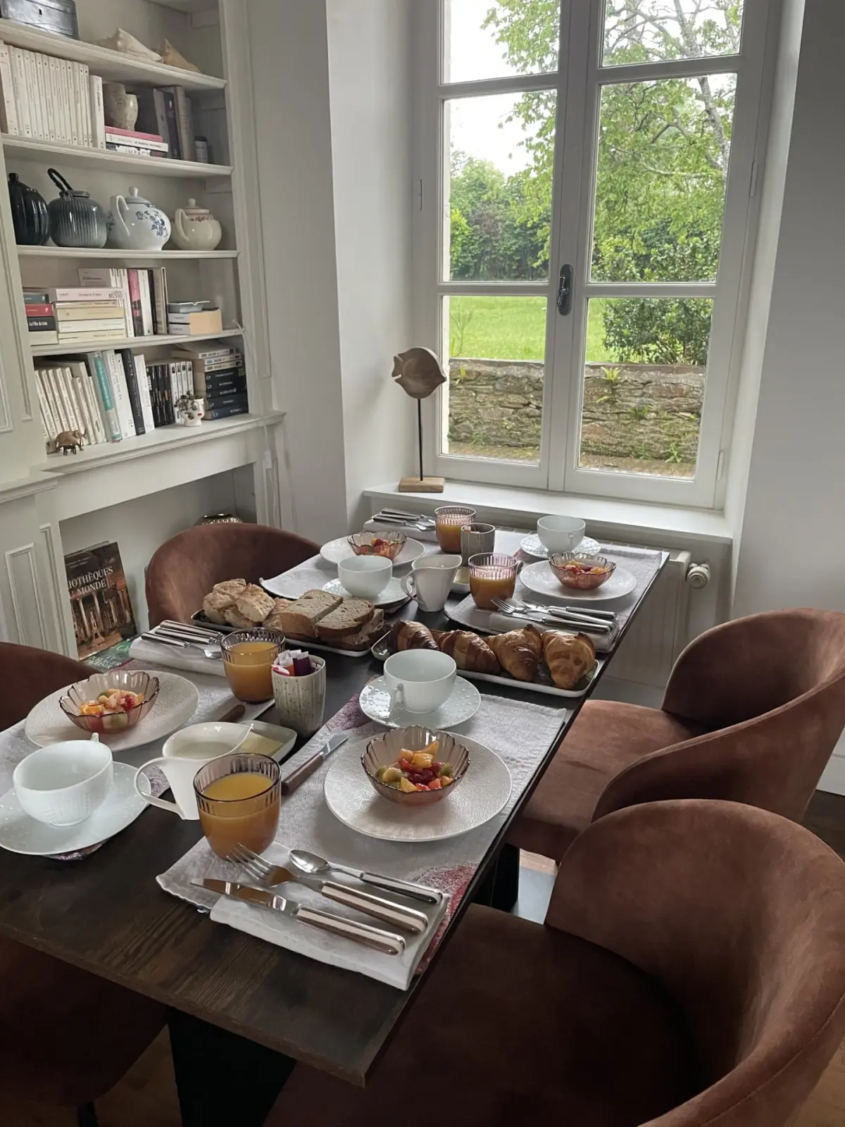 Breakfast table at Domaine de Marculfo by a window onto the garden, velvet chairs and bookcase