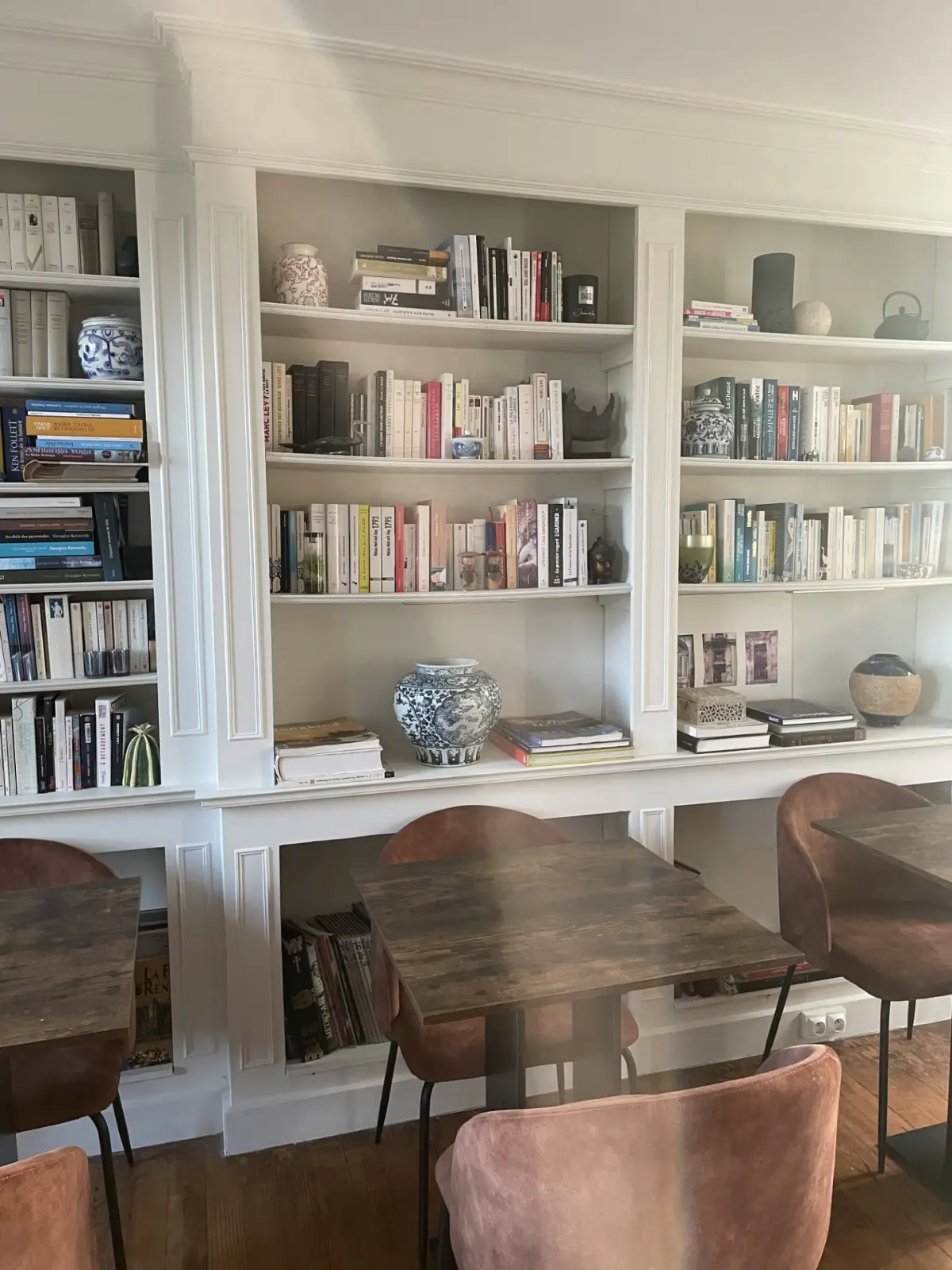 Room at Domaine de Marculfo, white built-in bookcase filled with books and china, tables and pink chairs