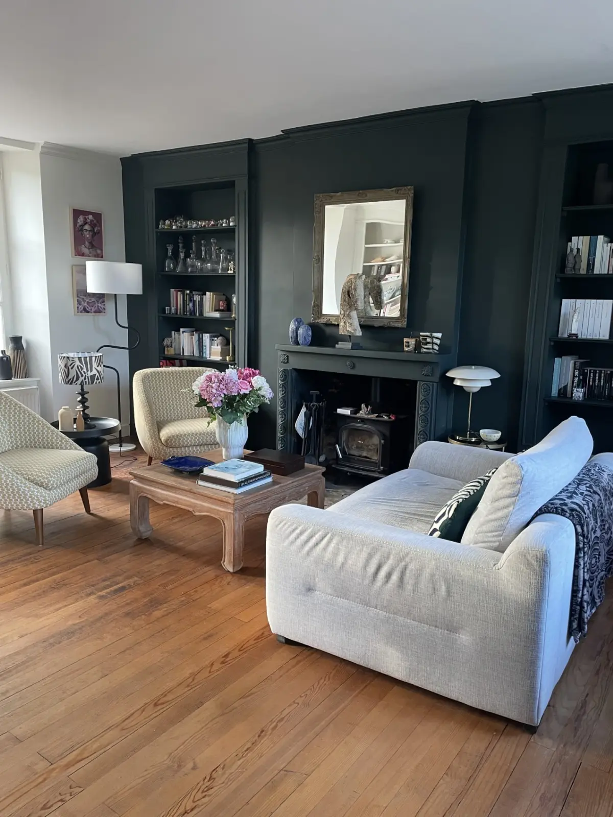 Living room at Domaine de Marculfo: white sofa, wood-burning stove, dark green walls and built-in bookcases
