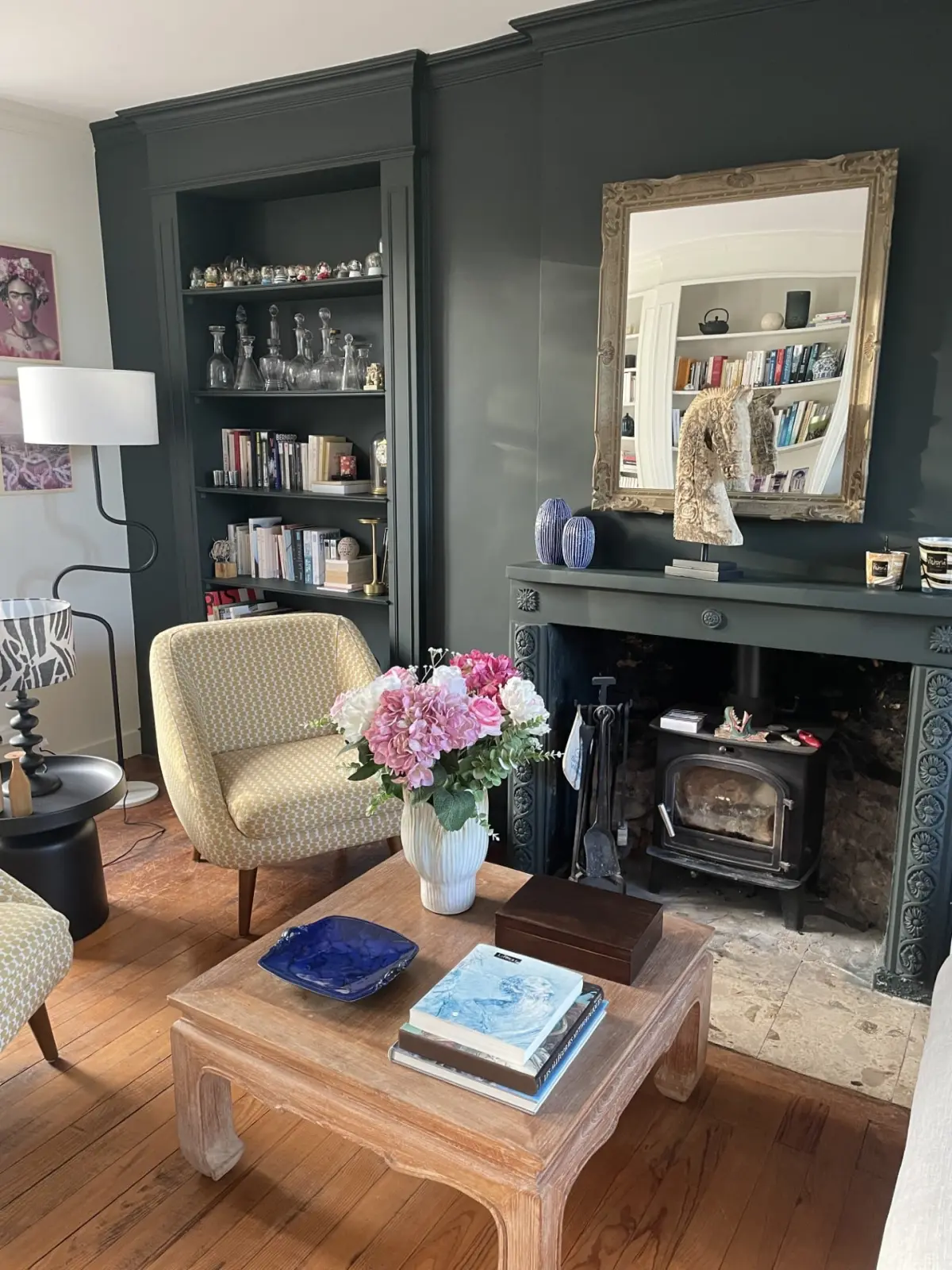 Corner of the Domaine de Marculfo living room with armchair, wood-burning stove, gilt mirror and peonies
