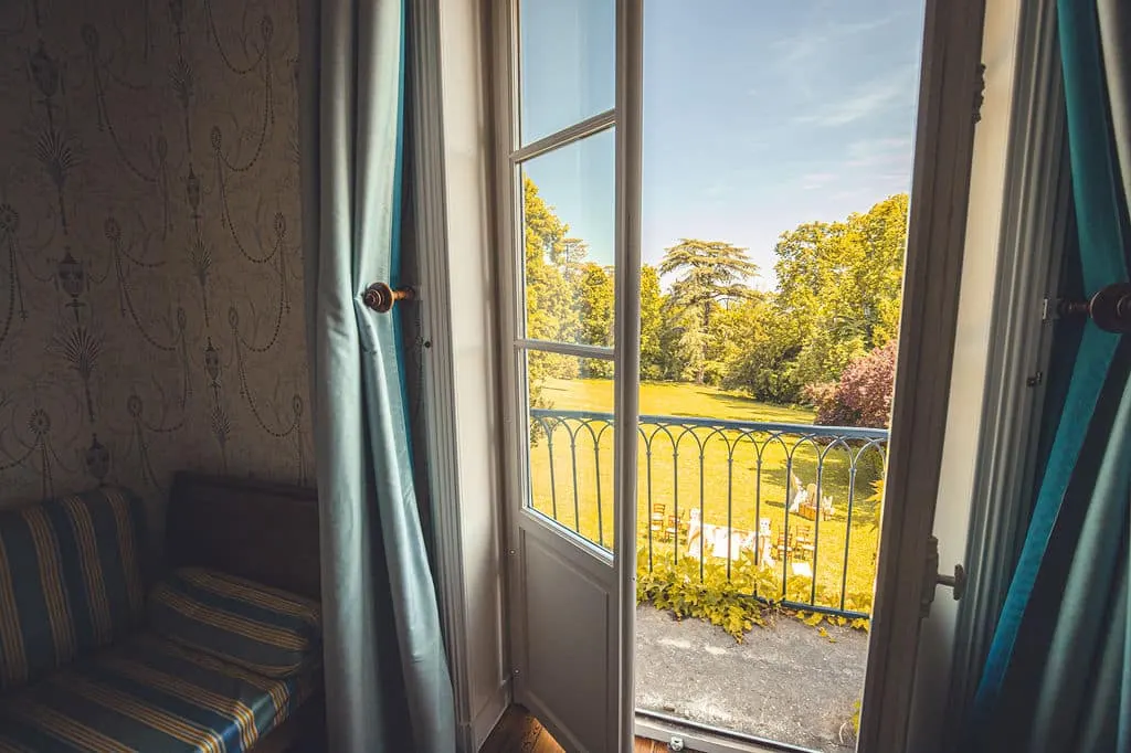 French window in the Marie bedroom opening onto a wrought-iron balcony and the Domaine de Montclair lawn