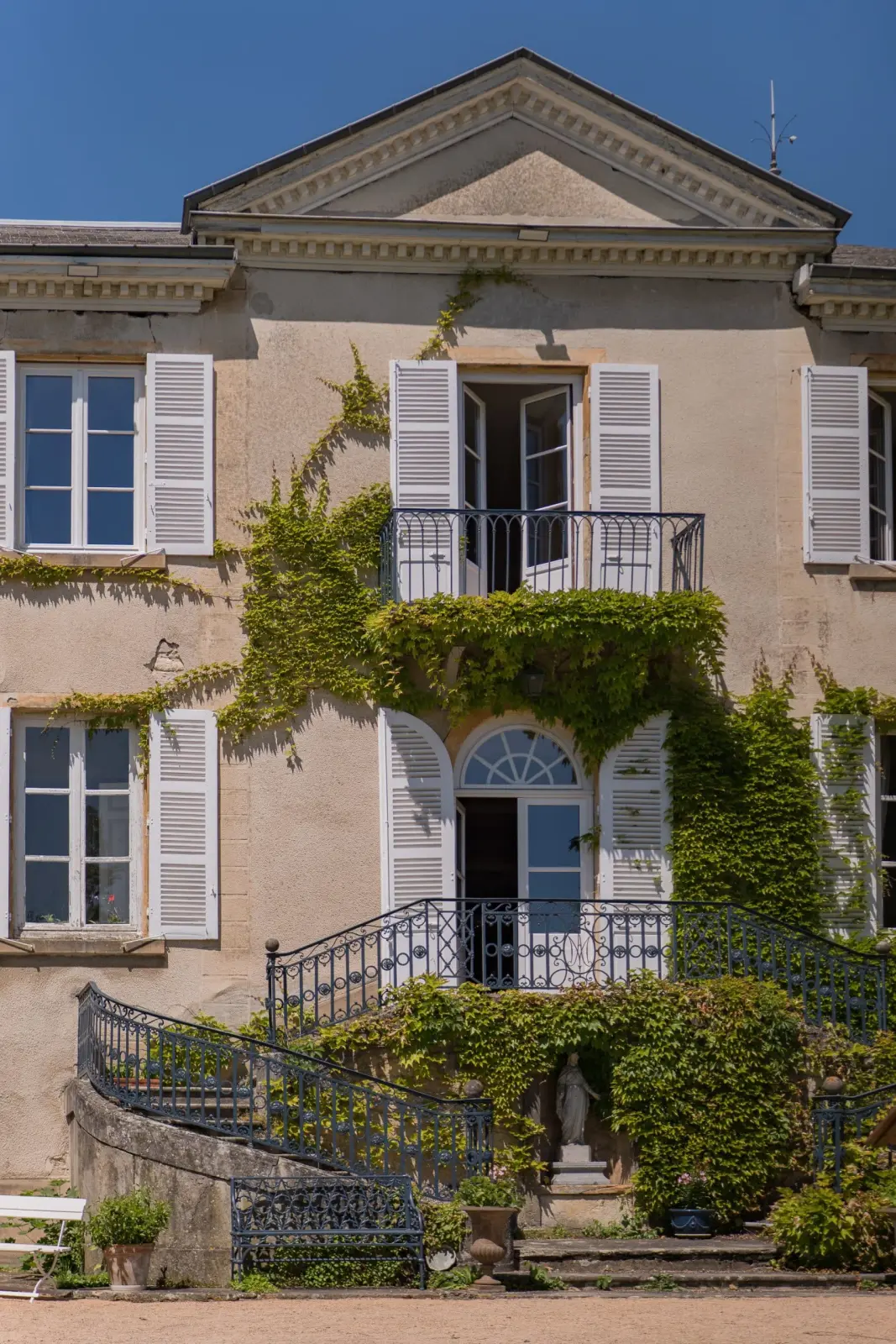 Façade of Domaine de Montclair covered in Virginia creeper, with a pediment and twin wrought-iron staircase