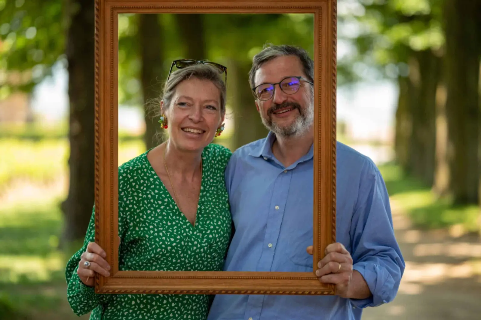 The Domaine de Montclair host couple posing inside a gilt frame in a tree-lined avenue