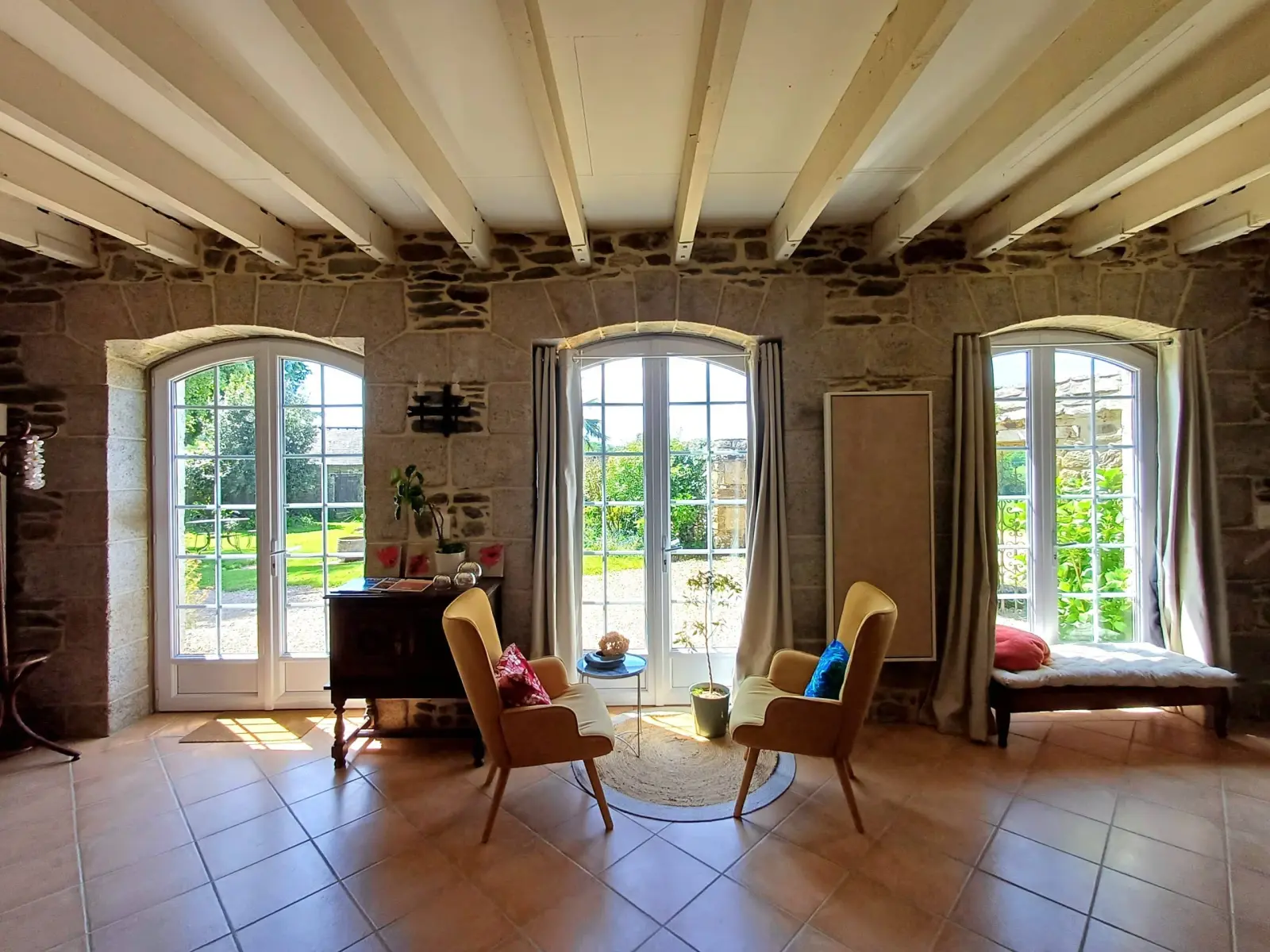 Sitting room with stone walls and white beams, three arched French windows and two yellow armchairs, Ty Monde