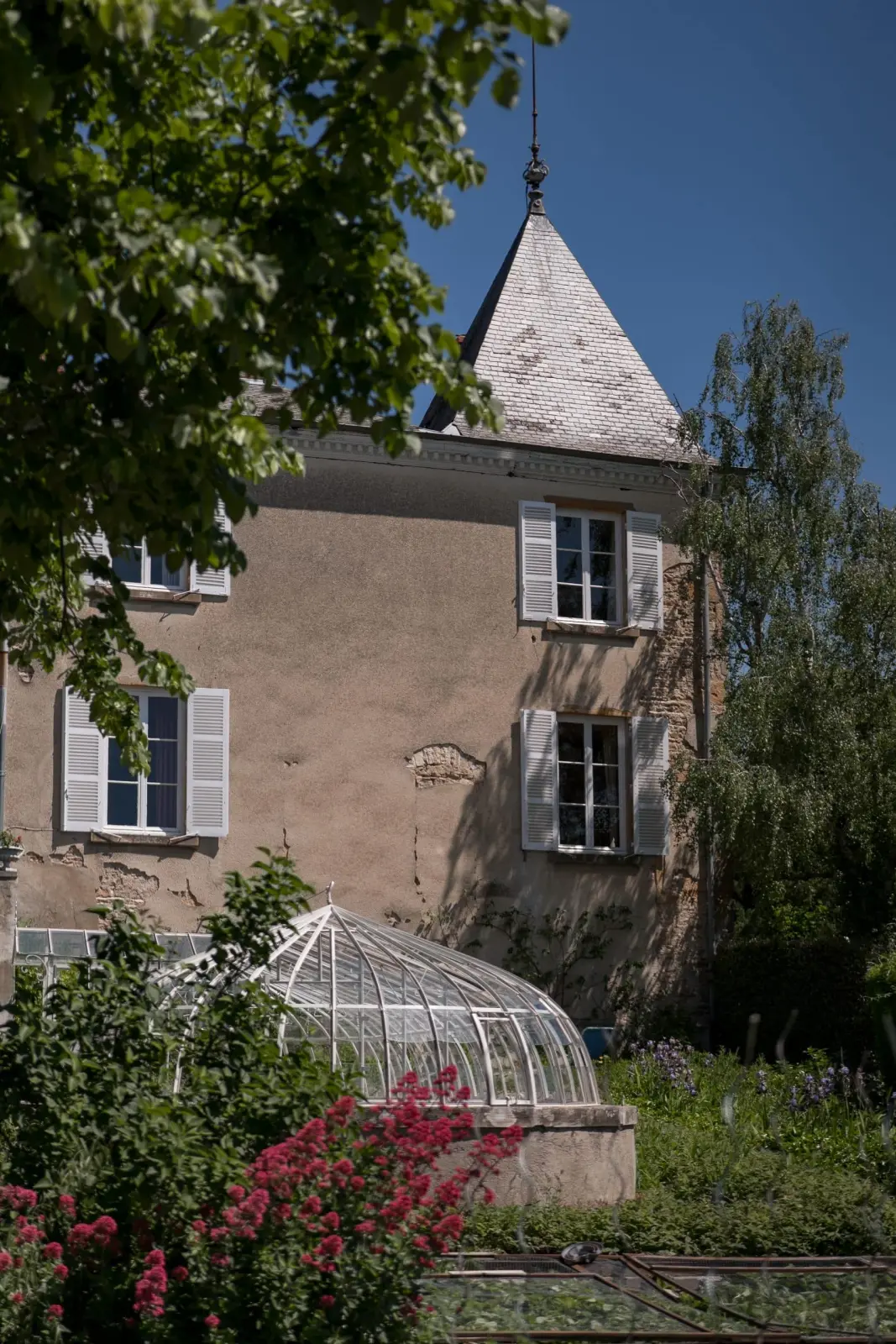 Pointed-roof tower of Domaine de Montclair and an old glass greenhouse in the flowering garden