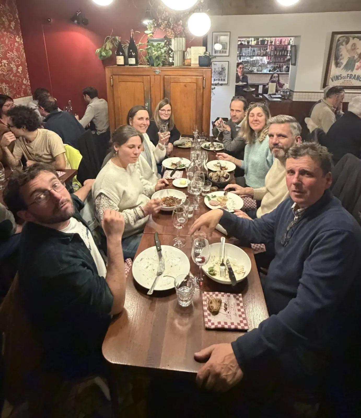Guests seated at a long restaurant table during a dinner, with plates and glasses