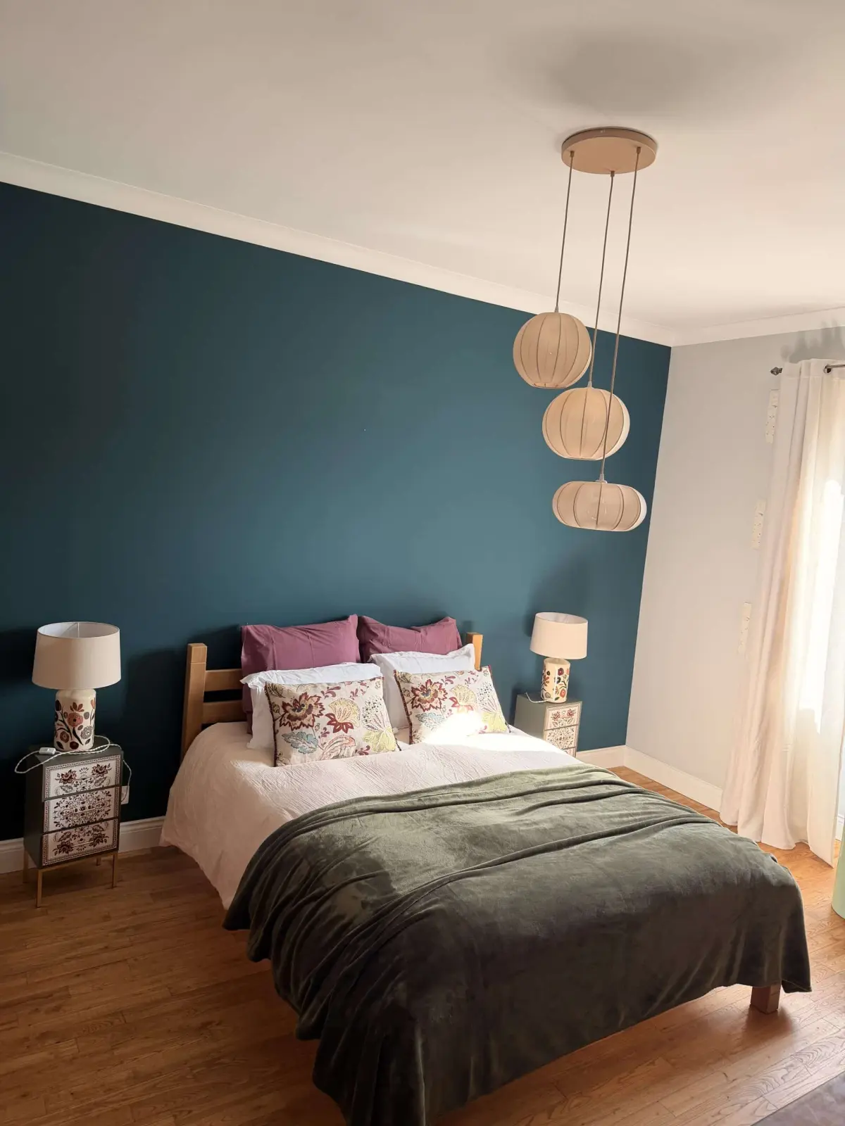 Bedroom at Le Patio Bleu with a double bed, plum cushions, teal wall and paper pendant lamps