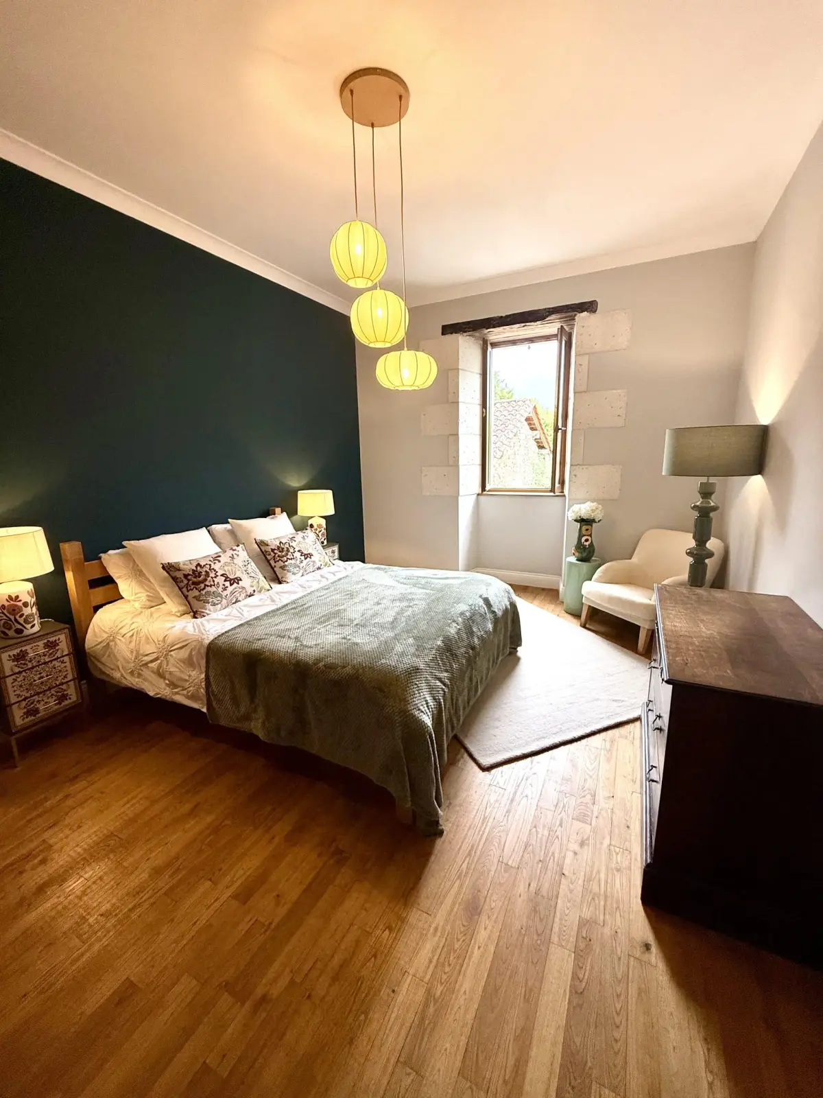 Bedroom at Le Patio Bleu with a teal wall, double bed, paper pendant lamps, wooden floor and window